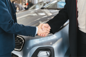 Two people shaking hands in front of a car.