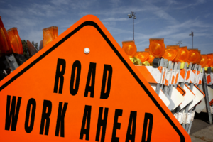 "Road Work Ahead" and other construction signs lined up on a road.