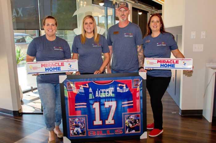 Signed Josh Allen jersey with Remax employees smiling next to it.