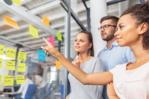 Three young professionals looking at sticky notes on a board.