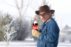 Cowboy standing outside holding a bottle of Coca Cola.