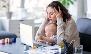 Stressed woman working at a computer with a baby on her lap.