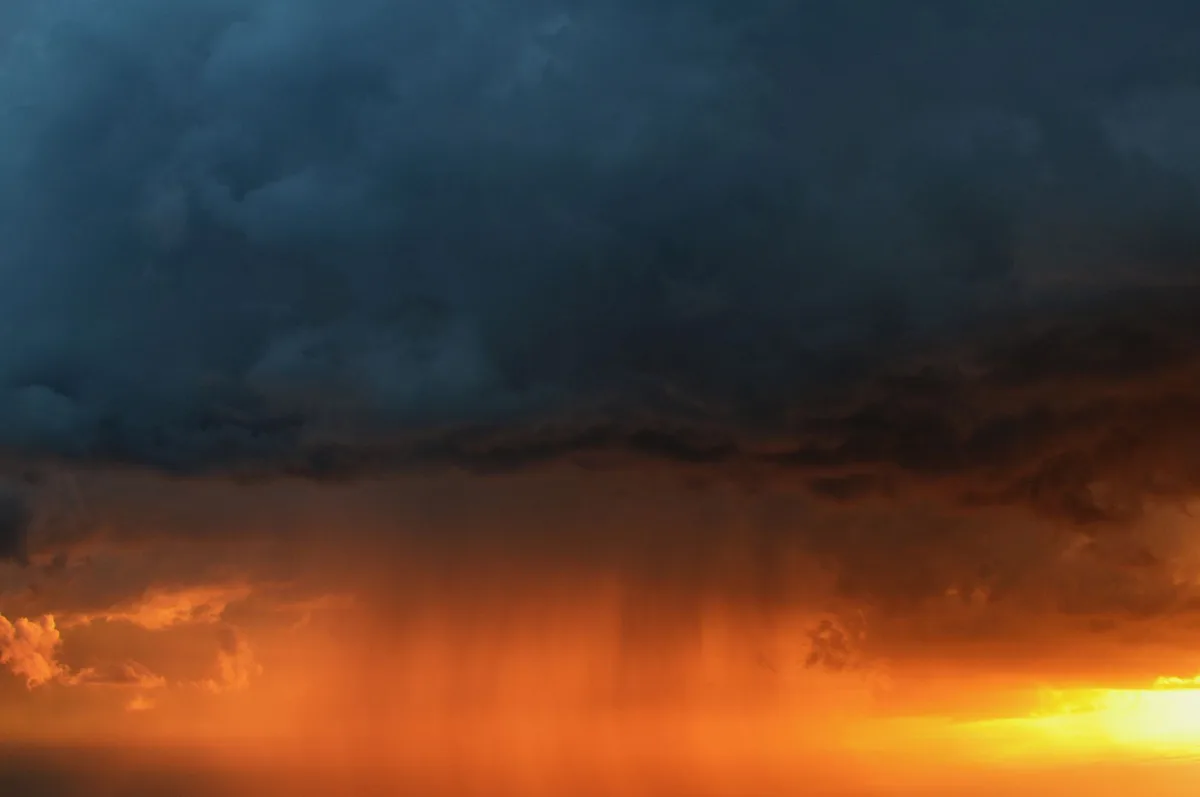 Dunkle Gewitterwolken nähern sich über flaches Gelände mit Regen in der Ferne