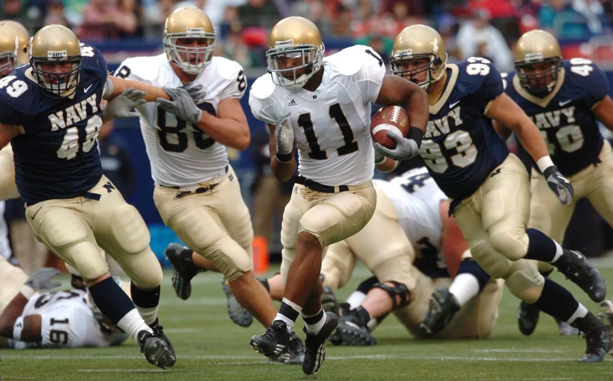 Running back carrying the football during a rushing play in a college football game.