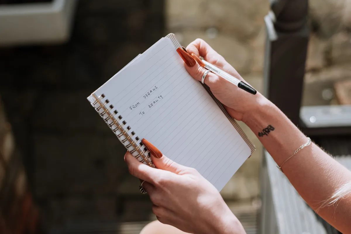 A hand holding a pen poised over an open notebook with soft light illuminating the page