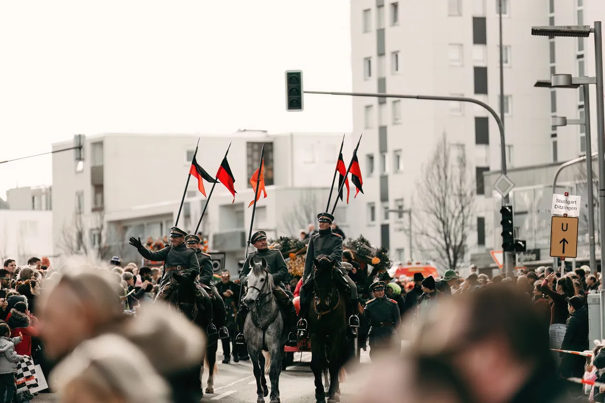Desfile militar con uniformados marchando ante multitud de espectadores en calle de pueblo