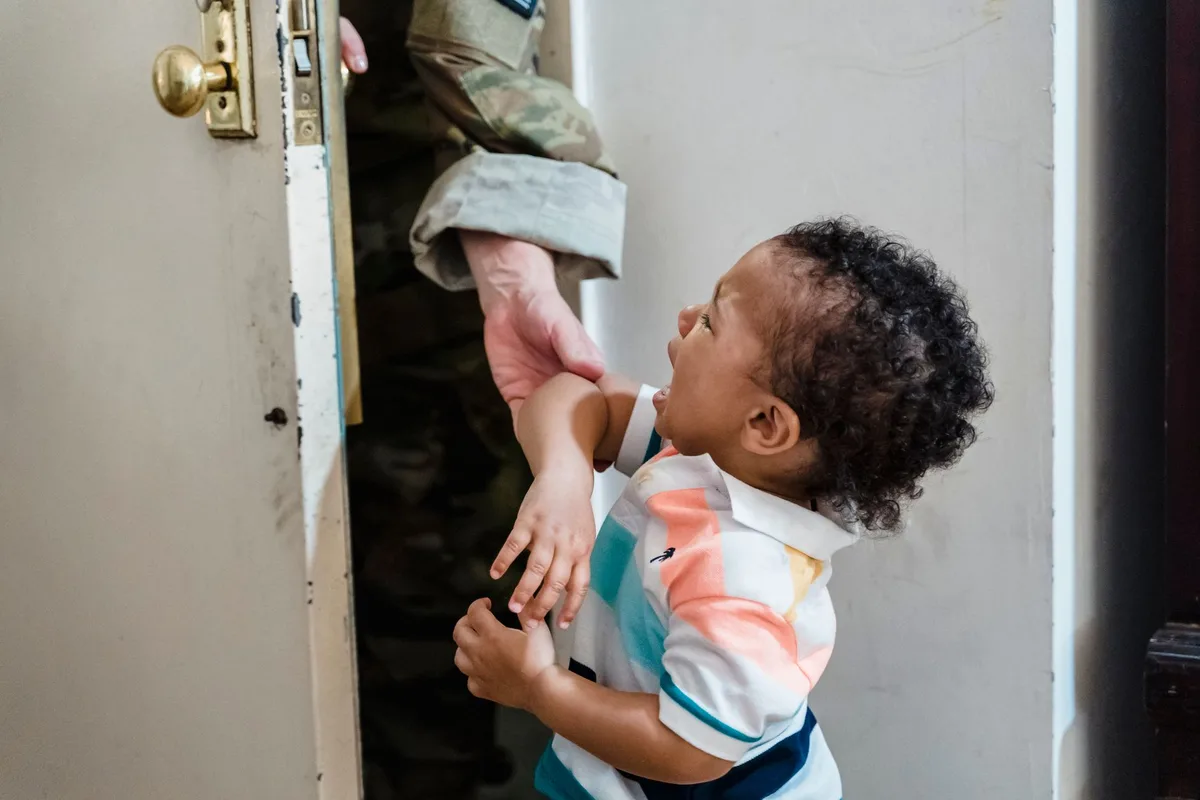 A service member in uniform dealing with childcare responsibilities at home, representing the operational impact of fami