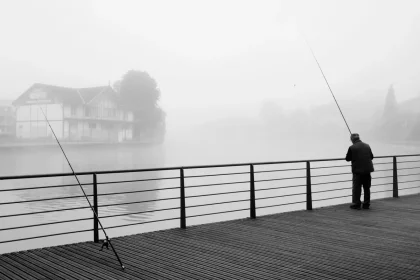 Angler fishing in river at sunrise with morning mist and trees