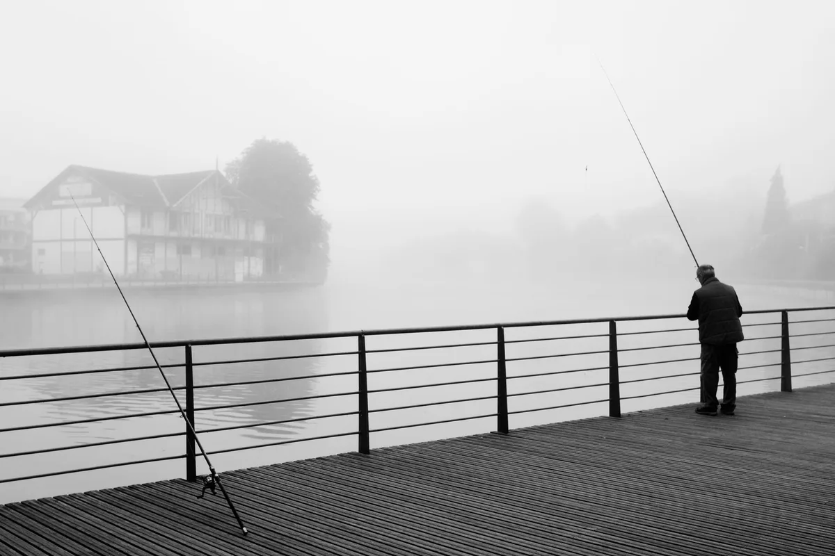 Angler fishing in river at sunrise with morning mist and trees