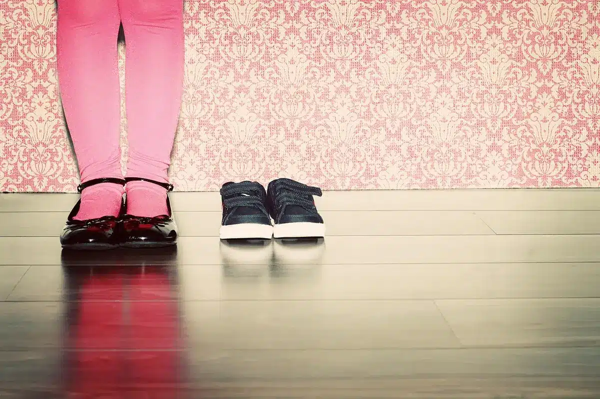Pair of children's shoes by a hallway with a coat on a hook, anonymous figure in background