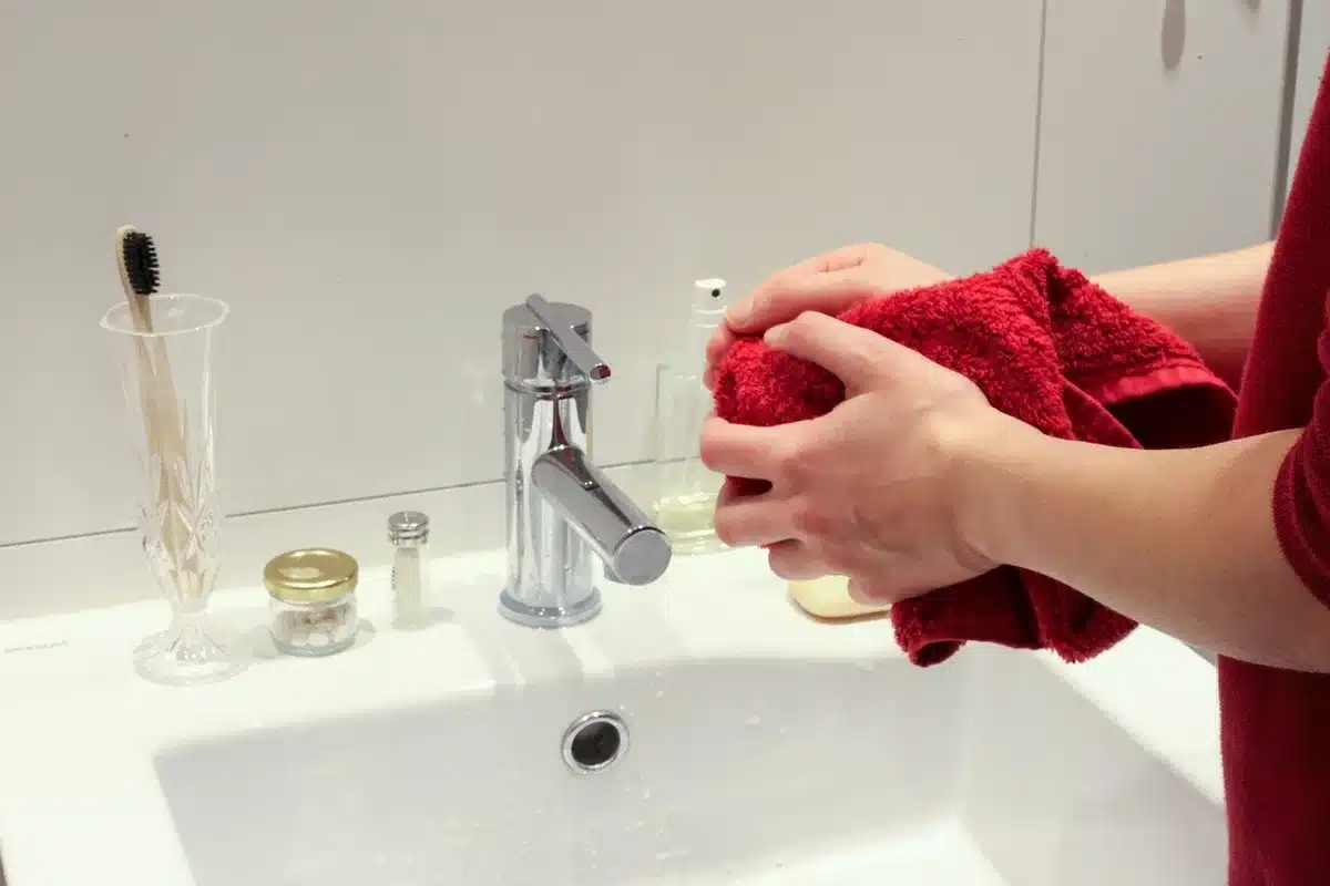 Hands reaching for a towel and bottle on a fogged bathroom shelf in soft light
