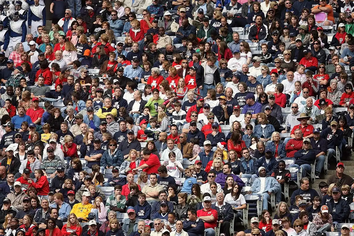 Sideline view of a college stadium with scoreboard and anonymous fans