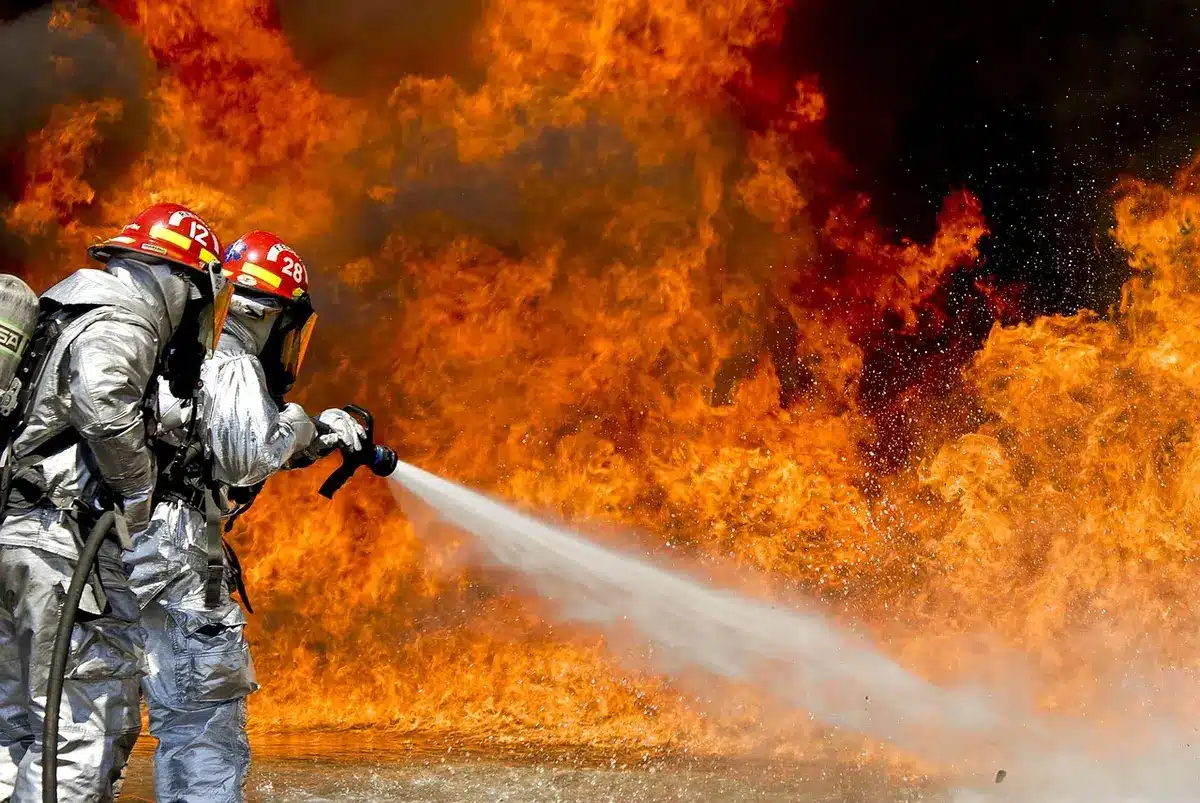 Firefighters directing hose at a burning dumpster near a garage