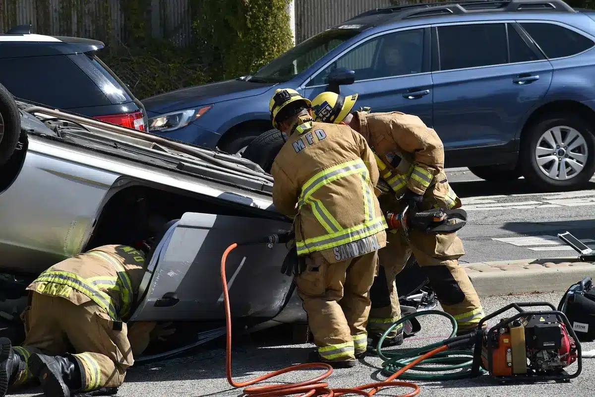 Emergency responders assisting injured passengers beside crashed pickup, seat belts visible
