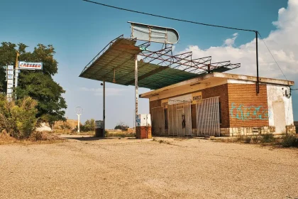 Empty gas station forecourt with pumps and a distant car near a highway