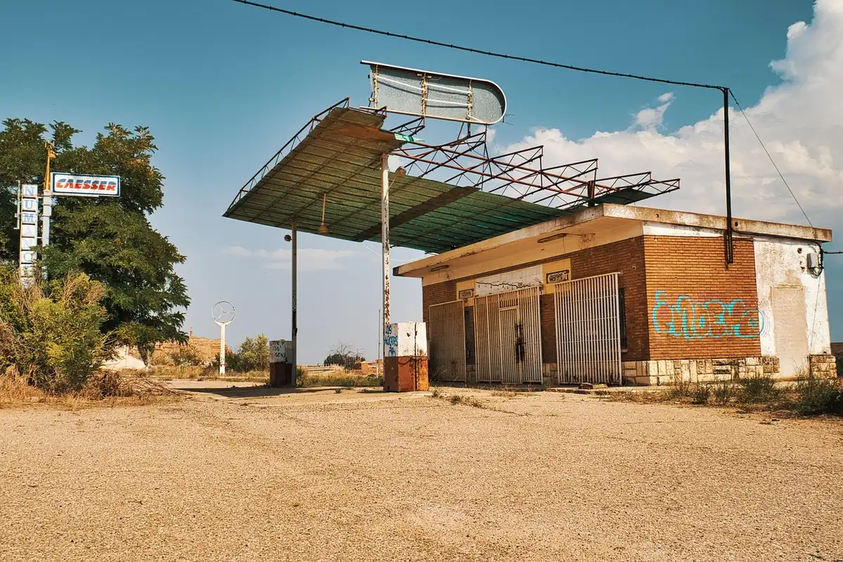 Empty gas station forecourt with pumps and a distant car near a highway